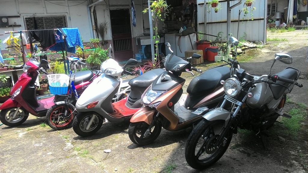 A row of scooters and motorcycles in front of an old house in Taiwan.