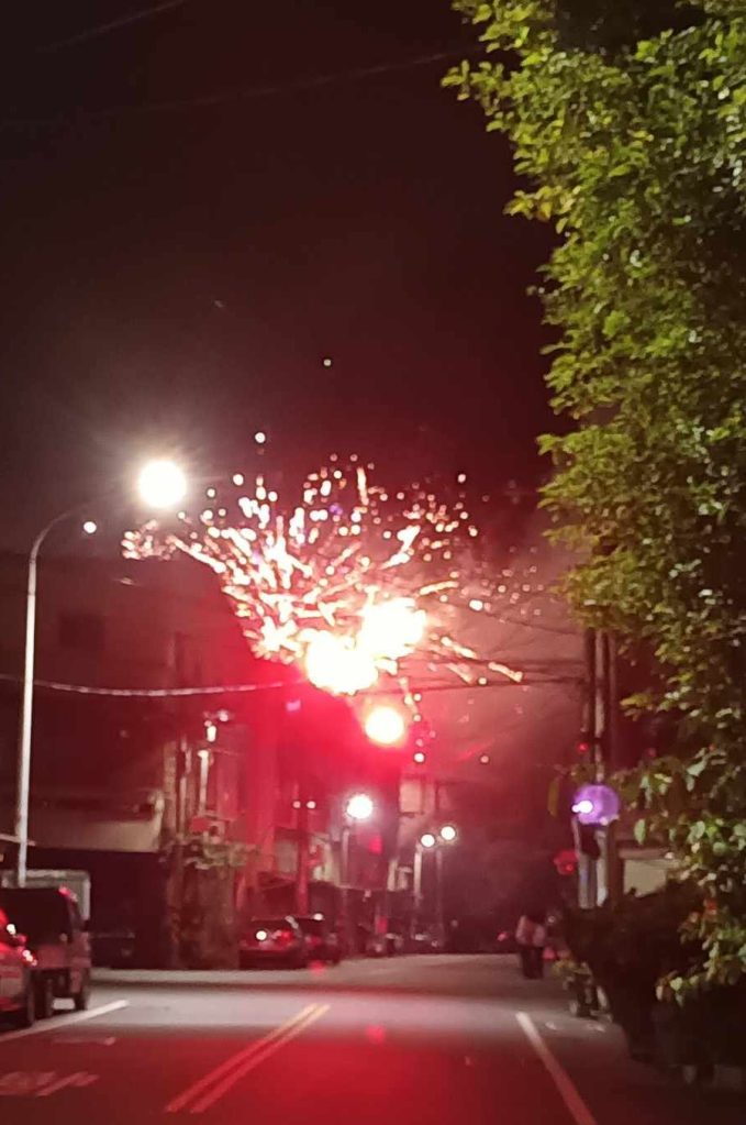 Fireworks explode above a house down the street.